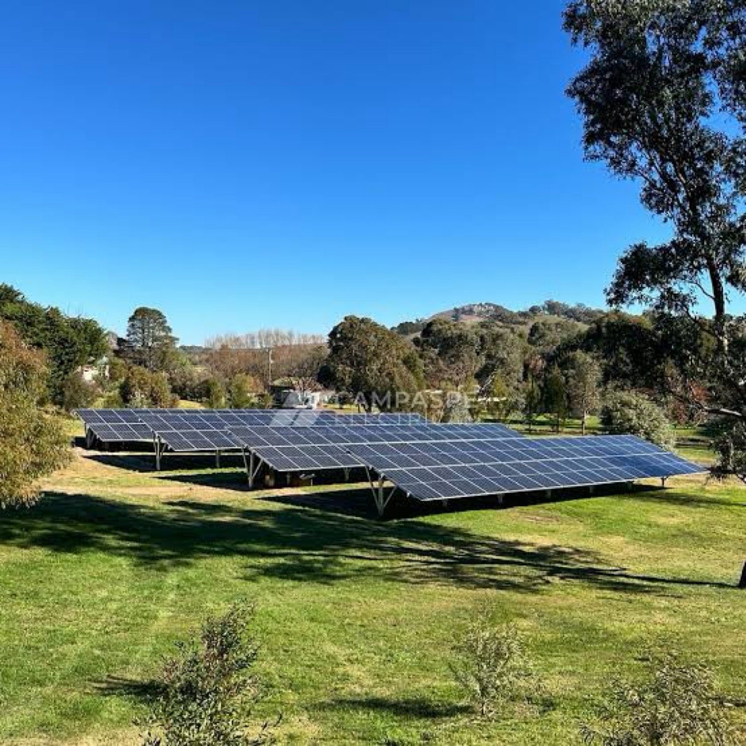 Ground-mount solar array on a grassy rural property with hills